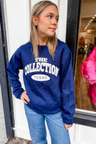 Person wearing a blue sweatshirt with 'The Collection Texas' text, standing in front of a store window.